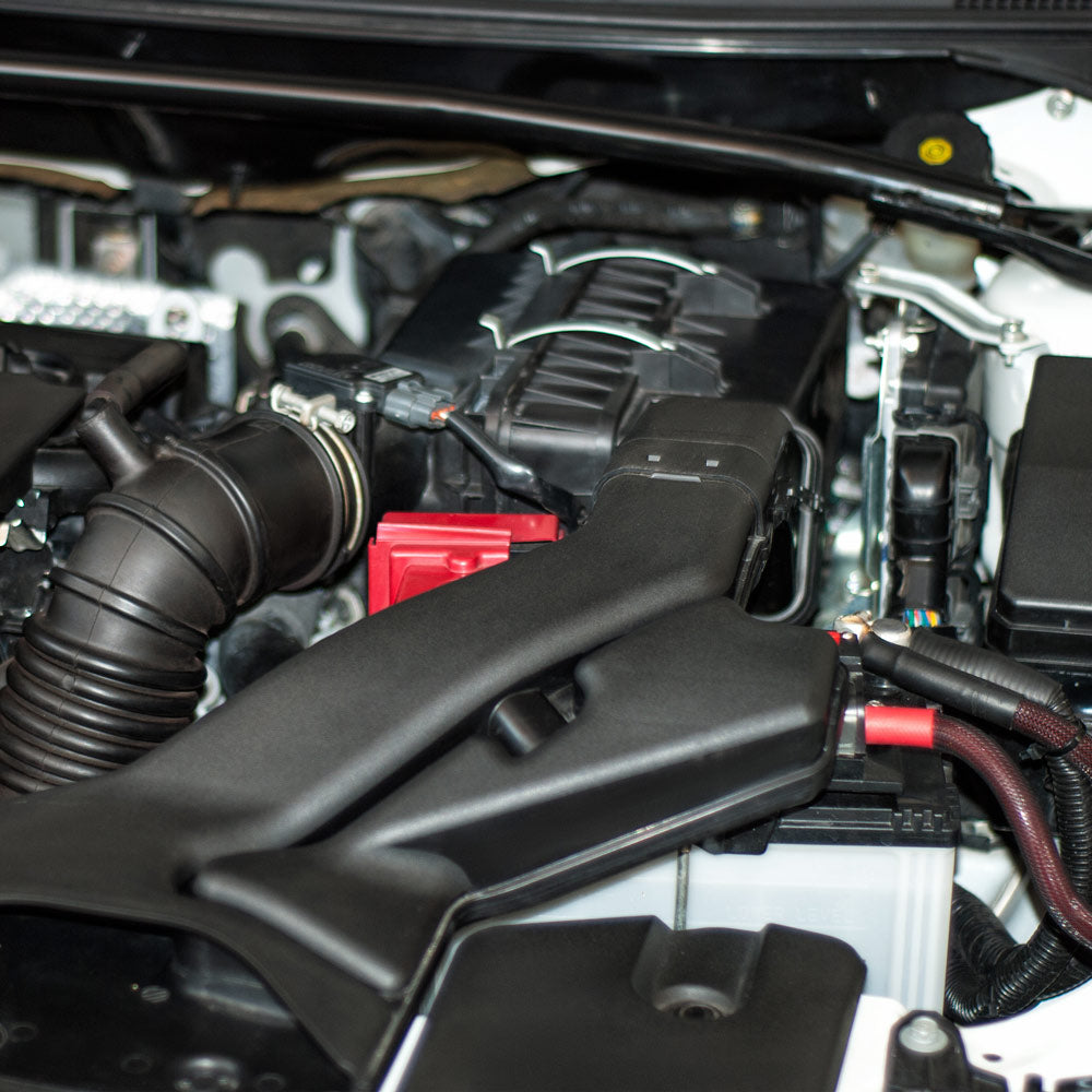 Nahaufnahme des Motorraums eines Autos, in der verschiedene Komponenten zu sehen sind, darunter Luftansaugrohre, Schläuche und elektrische Leitungen.