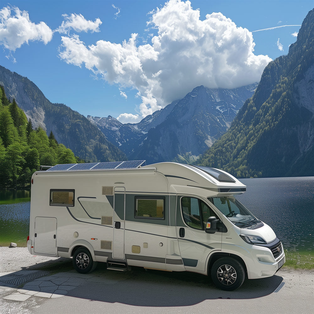 Ein weißes Wohnmobil mit Solarzellen auf dem Dach steht neben einem ruhigen See mit einer Berglandschaft im Hintergrund. Die Szene zeigt üppige grüne Bäume, dramatische Gipfel und einen hellen, mit Wolken übersäten Himmel.